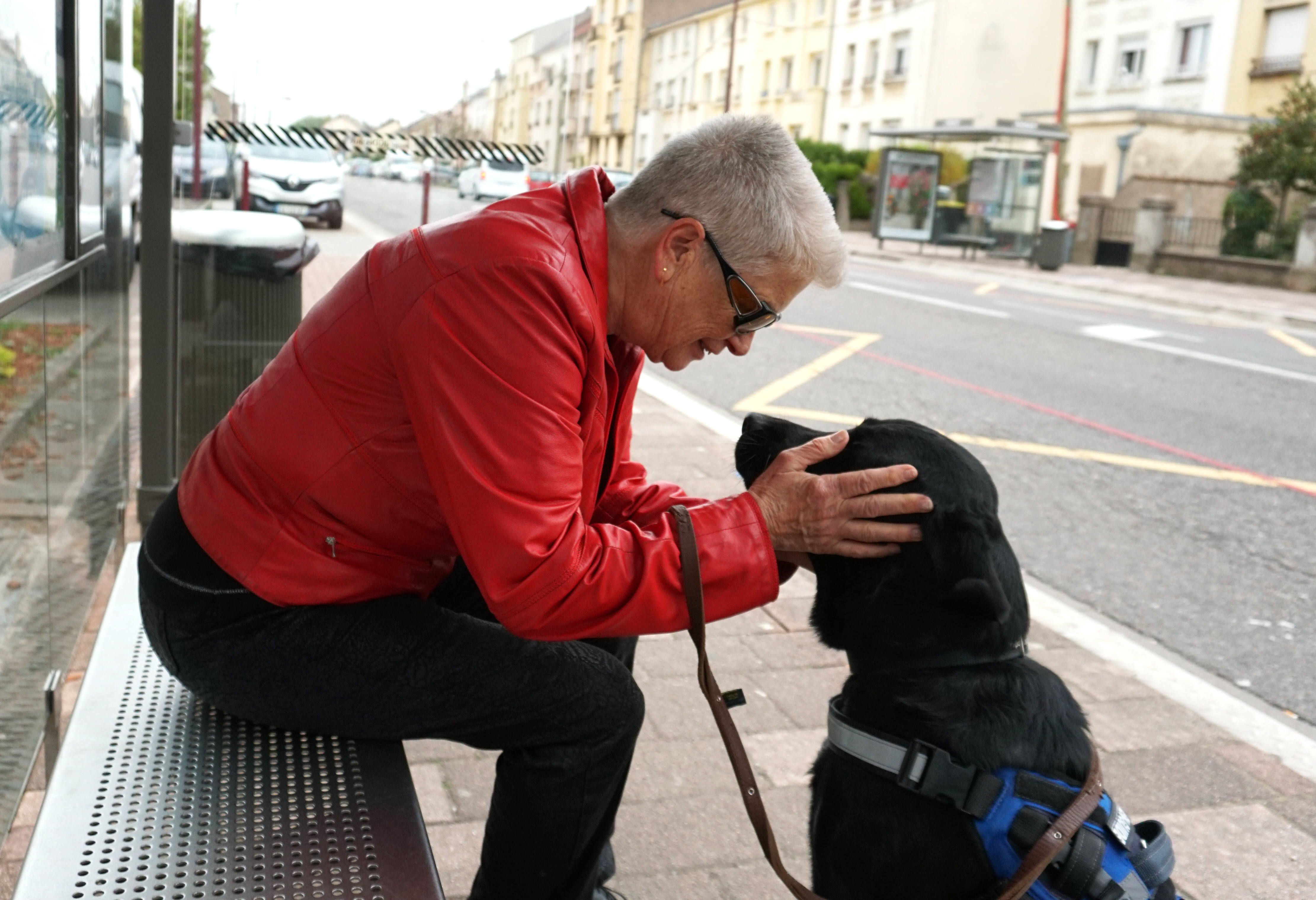 Femme assise sur un arret de bus tenant la tête d'un chien noir